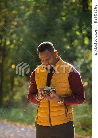 African american guy photographer taking picture with vintage camera on city green park - leisure activity, diversity and hobby concept African american guy photographer taking picture with vintage camera on city green park - leisure activity, diversity and hobby concept 98603666