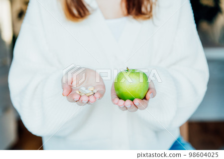 Female hands with green apple and different pills. Choose between natural, folk and traditional synthetic way of vitamins, health care. Diet modification, diabetes management, drugs alternative. Female hands with green apple and different pills. Choose between natural, folk and traditional synthetic way of vitamins, health care. Diet modification, diabetes management, drugs alternative. 98604025