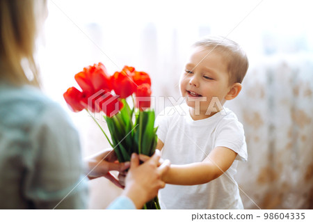 Little son congratulates mother, gives bouquet of flowers tulips. Happy mother's day. Family holiday Little son congratulates mother, gives bouquet of flowers tulips. Happy mother's day. Family holiday 98604335