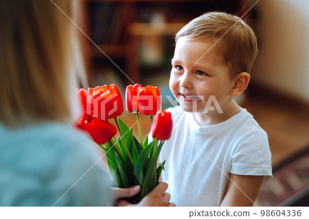 Little son congratulates mother, gives bouquet of flowers tulips. Happy mother's day. Family holiday Little son congratulates mother, gives bouquet of flowers tulips. Happy mother's day. Family holiday 98604336
