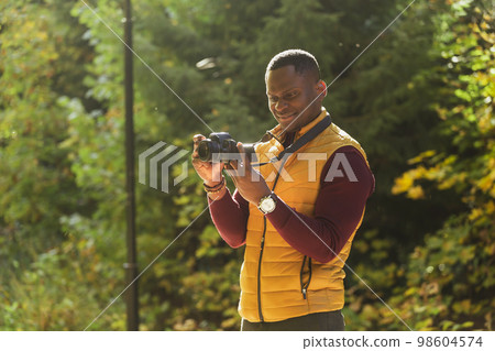 Close-up african american guy photographer taking picture with photo camera on city green park copy space and place for text - leisure activity, diversity and hobby concept Close-up african american guy photographer taking picture with photo camera on city green park copy space and place for text - leisure activity, diversity and hobby concept 98604574