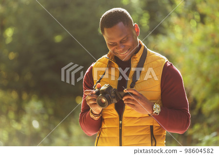 African american guy photographer taking picture with vintage camera on city green park - leisure activity, diversity and hobby concept African american guy photographer taking picture with vintage camera on city green park - leisure activity, diversity and hobby concept 98604582