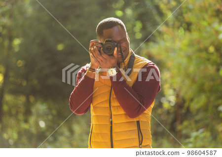 African american guy photographer taking picture with photo camera on city green park portrait - leisure activity, diversity and hobby concept 98604587