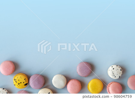 Many different macaroons on blue background with copy space. Pink, white and violet French cookies. Strawberry, black currant and blueberry vanilla meringue dessert 98604759