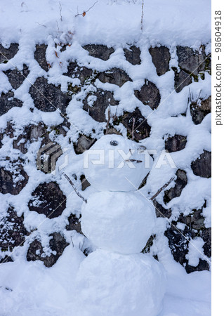 A snowman made in front of a stone wall 98604918