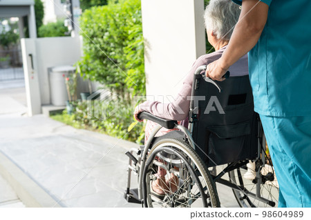 Caregiver help and care Asian senior or elderly old lady woman patient sitting in wheelchair on ramp at nursing hospital, healthy strong medical concept 98604989