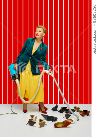 Creative portrait of fashionable middle age blonde woman with short haircut in stylish clothes among retro interior objects over bright color background. 98605256
