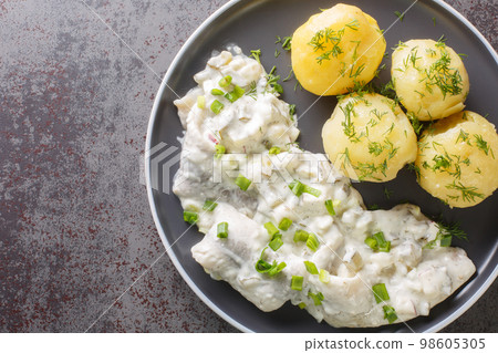 Herring fillet with apples, pickles, onions in a creamy sauce with a side dish of boiled potatoes close-up in a plate. horizontal top view Herring fillet with apples, pickles, onions in a creamy sauce with a side dish of boiled potatoes close-up in a plate. horizontal top view 98605305