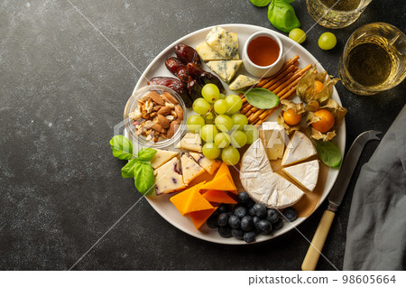 Cheese plate with various cheeses, fruits, nuts and snacks. Dark background, copy space Cheese plate with various cheeses, fruits, nuts and snacks. Dark background, copy space 98605664