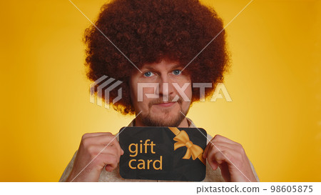 Young happy man showing pointing gift discount certificate voucher coupon for store holidays sale Young happy man showing pointing gift discount certificate voucher coupon for store holidays sale 98605875