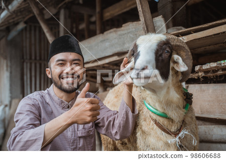 a man squatting in front of the goat's stable with thumb up a man squatting in front of the goat's stable with thumb up 98606688