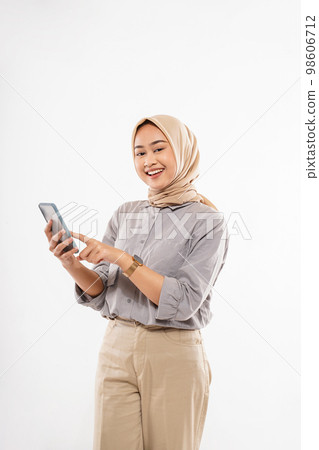 a young woman with hijab standing and pointing on her phone 98606712