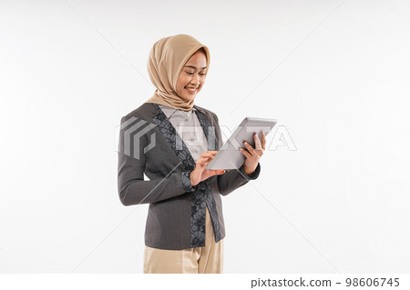 a woman with hijab and gray blazzer standing looking at the tablet 98606745