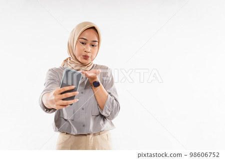 woman with hijab standing raise her hand and blowing on her phone 98606752