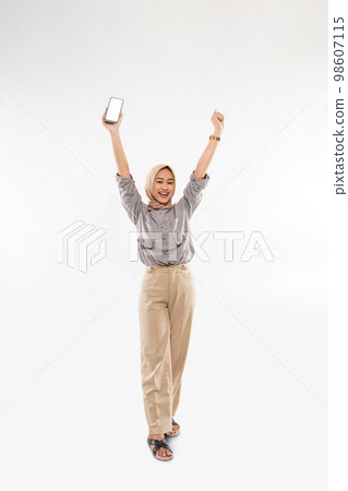 a moslem woman in shirt and long pants standing raising her arms 98607115