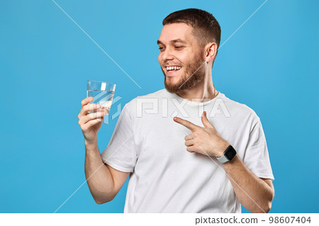 happy handsome man in white t-shirt showing drinking glass of water 98607404
