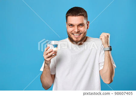 man in white t-shirt with raised arm holding glass of water 98607405