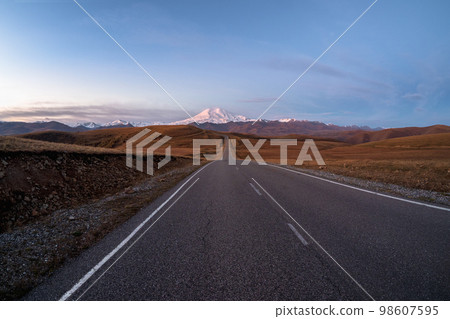 Morning highway to the snow-capped peaks. Autumn morning deserted highway. Beautiful asphalt freeway, motorway, highway through of caucasian landscape mountains hills. Morning highway to the snow-capped peaks. Autumn morning deserted highway. Beautiful asphalt freeway, motorway, highway through of caucasian landscape mountains hills. 98607595