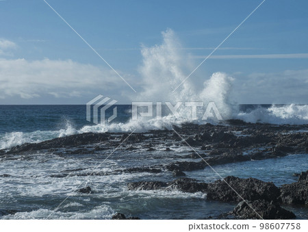 Big waves splash against black lava rock in the Atlantic Ocean near Los Gigantes, Tenerife, Canary islands, Spain. Sunny winter day. 98607758