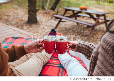 Hot cups of tea in hands in woollen sweater on background of cozy house Hot cups of tea in hands in woollen sweater on background of cozy house 98608275