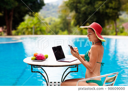 Woman with laptop at swimming pool. Remote work. 98609000