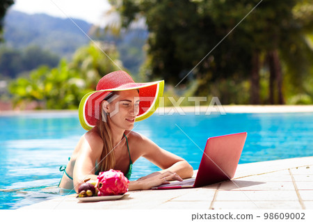 Woman with laptop at swimming pool. Remote work. 98609002