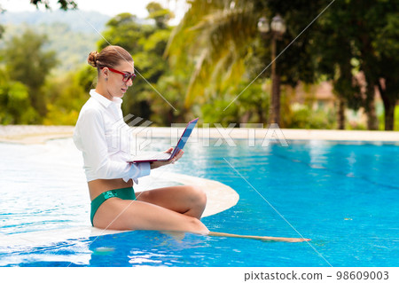 Woman with laptop at swimming pool. Remote work. 98609003