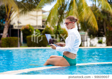 Woman with laptop at swimming pool. Remote work. 98609007