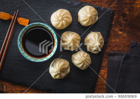 Xiaolongbao, traditional steamed dumplings and soy sauce. Xiao Long Bao buns on cutting board. Top view. 98609069