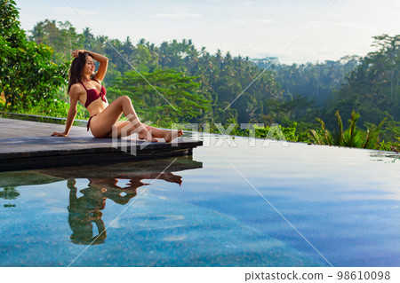 Young woman in swimming pool with tropical jungle view 98610098