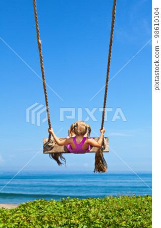 Happy girl have fun swinging high on sea beach Happy girl have fun swinging high on sea beach 98610104