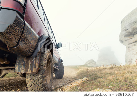 Close-up detail bottom POV view of 4x4 awd suv vehicle on dirt gravel unpaved road in autumn at misty mountain top. Off road car mountain safari adventure nature trial journey concept. ATV rental 98610167