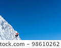 A climber in a red suit climbs an icy white mountain 98610262