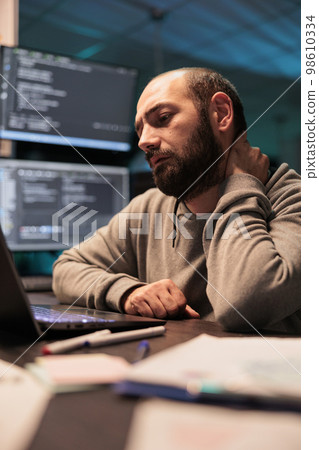 Tired app developer dealing with back pain and pressure, working late at night and feeling tense. Exhausted stressed programmer coding html script and feeling overworked, neck tension. 98610334