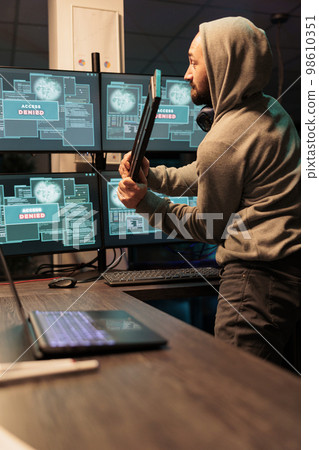 Displeased angry hacker throwing keyboard in office, feeling mad about hacking system failure. Dealing with hardware error and trying to steal server information, violent thief. 98610351
