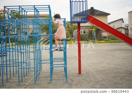 Girl playing on jungle gym in park Girl playing on jungle gym in park 98610443