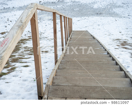 Wooden ladder in the snow. Descent to the water. 98611097
