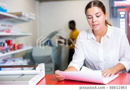 Focused young woman in white shirt checking the print quality and accepting color proofs in typography Focused young woman in white shirt checking the print quality and accepting color proofs in typography 98611963