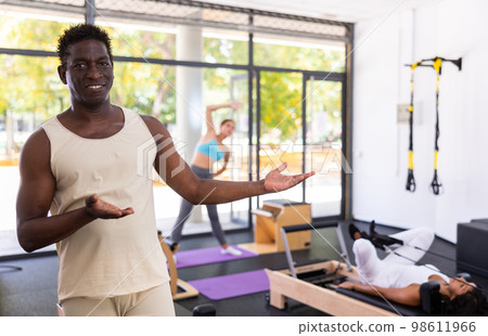 Portrait of African American male fitness instructor inviting to pilates reformer studio Portrait of African American male fitness instructor inviting to pilates reformer studio 98611966