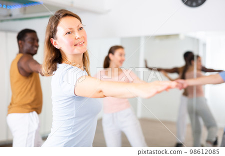 Smiling young adult couples dancing together in pairs and practicing movements in modern choreography class Smiling young adult couples dancing together in pairs and practicing movements in modern choreography class 98612085