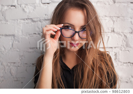 beautiful girl close-up in the glasses smiles against the background of a white wall beautiful girl close-up in the glasses smiles against the background of a white wall 98612803