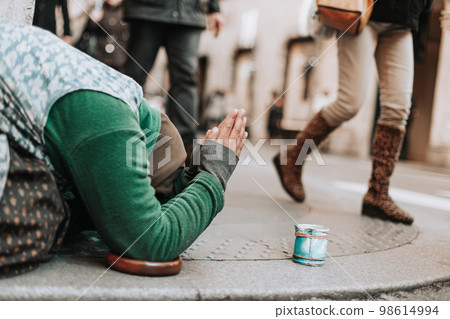 a woman on her knees begs for alms on a city street. a woman on her knees begs for alms on a city street. 98614994