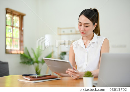 Beautiful millennial Asian businesswoman focusing on her business tasks on digital tablet 98615702