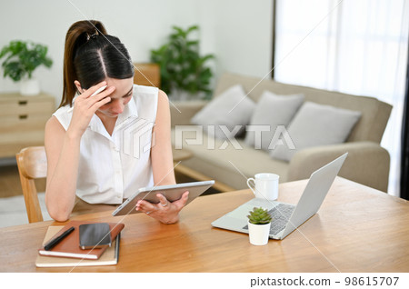Stressed and thoughtful Asian businesswoman working from home, managing her tasks on tablet Stressed and thoughtful Asian businesswoman working from home, managing her tasks on tablet 98615707
