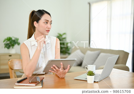Thoughtful Asian businesswoman working from home, using tablet Thoughtful Asian businesswoman working from home, using tablet 98615708