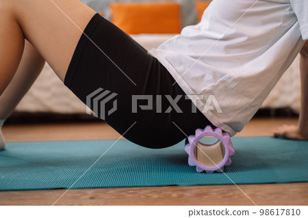 Lady gives herself a lower back massage with a purple massage roller Lady gives herself a lower back massage with a purple massage roller 98617810