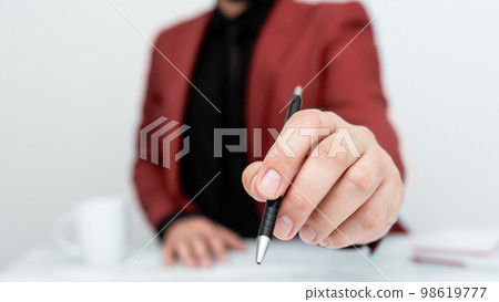 Male model in Red suit sitting at white table And Pointing With Pen On Important Message. Gentleman Showing Critical Announcement. Coffee cup on deck. Male model in Red suit sitting at white table And Pointing With Pen On Important Message. Gentleman Showing Critical Announcement. Coffee cup on deck. 98619777