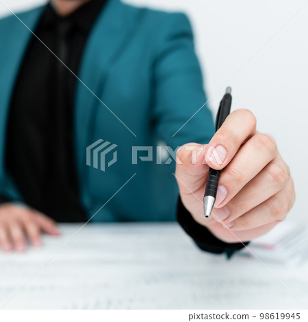Male model in Blue suit sitting at white table And Pointing With Pen On Important Message. Gentleman Showing Critical Announcement. Coffee cup on deck. Male model in Blue suit sitting at white table And Pointing With Pen On Important Message. Gentleman Showing Critical Announcement. Coffee cup on deck. 98619945
