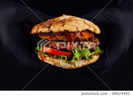 Man holds burger with nugget and cutlet in hands in black gloves Man holds burger with nugget and cutlet in hands in black gloves 98624483