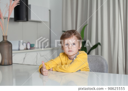 Smiling happy child boy in yellow sweater sitting by the table and showing thumb up 98625555